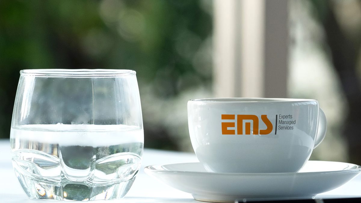 Eine EMS-Tasse neben einem Wasserglas.